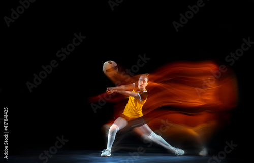 Young female volleyball player isolated on black studio background in mixed light. Woman in sportswear training and practicing in action. Concept of sport, healthy lifestyle, motion and movement.