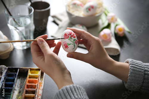 Woman painting Easter egg at black table, closeup photo