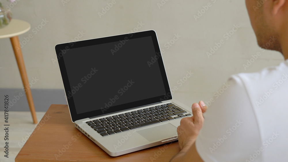 Man is looking for the laptop screen, grey wall background, open computer and table. Man is looking for the laptop screen, grey wall background, open computer and table.