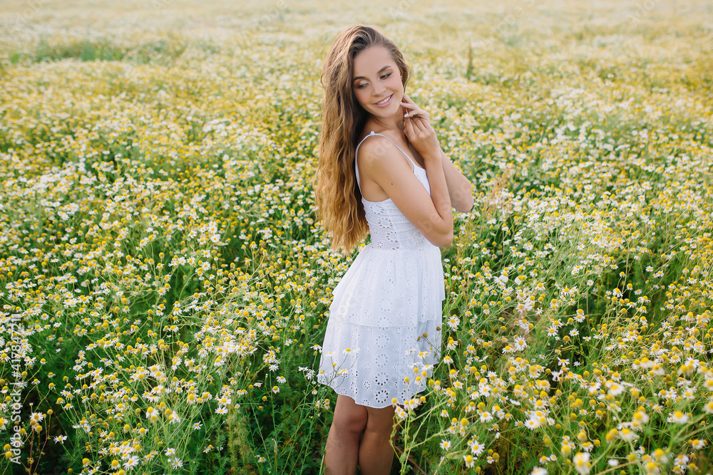 Very beautiful woman model stands in a field with daisies in a white dress with long hair Very beautiful woman model stands in a field with daisies in a white dress with long hair