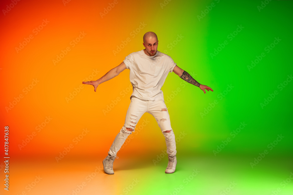 Naklejka premium Urban. Stylish sportive caucasian man dancing hip-hop on colorful gradient background at dance hall in neon light. Youth culture, movement, style and fashion, action. Fashionable bright portrait.