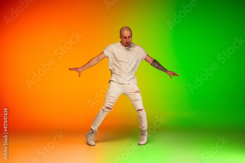 Urban. Stylish sportive caucasian man dancing hip-hop on colorful gradient background at dance hall in neon light. Youth culture, movement, style and fashion, action. Fashionable bright portrait.