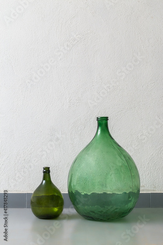 Green antique green glass demijohns to decor an interior, white wall and grey floor
