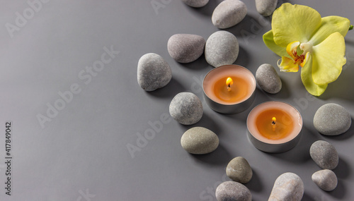 Aromatic  candles  orchid flower and stones on a gray background.  Spa composition. Relaxation and zen like concept..