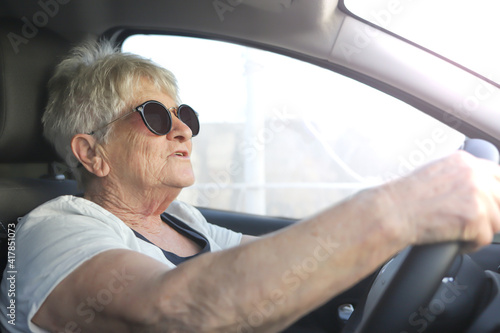 Happy senior woman in sunglasses driving automobile.