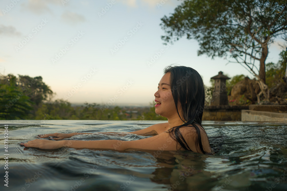 Fototapeta premium young woman relaxed at luxury resort infinity pool - happy and cheerful Asian Korean girl in bikini enjoying jungle view at hotel swimming pool during summer holidays travel