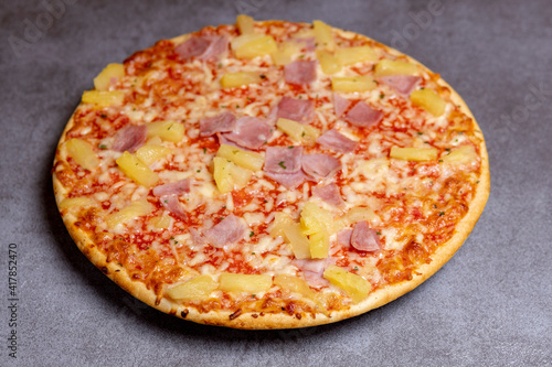 Modern kitchen gray surface with simple Hawai pineapple ham oven pizza with crunchy crest and golden yellow orange tint. Studio food still life against a seamless yellow background