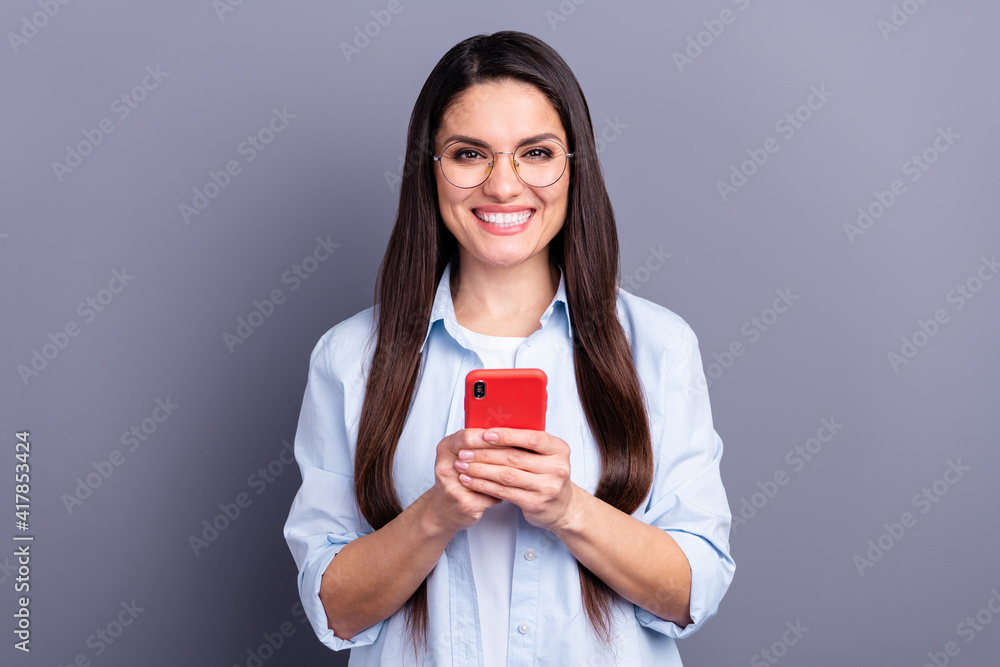Photo of adorable shiny young lady dressed blue shirt glasses communicating modern gadget isolated grey color background Photo of adorable shiny young lady dressed blue shirt glasses communicating modern gadget isolated grey color background