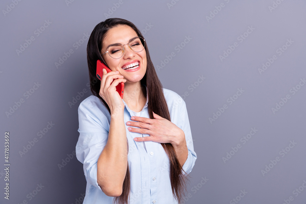 Photo of cute funny young lady dressed blue shirt glasses laughing arm chest talking modern gadget isolated grey color background Photo of cute funny young lady dressed blue shirt glasses laughing arm chest talking modern gadget isolated grey color background