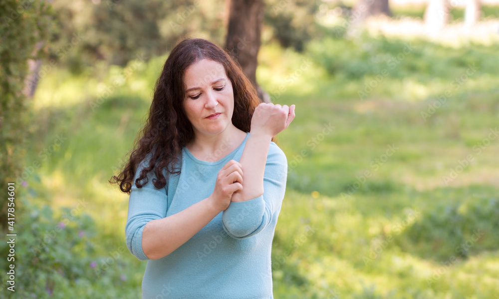 Woman scratching arm because it stings in a park with a green background Woman scratching arm because it stings in a park with a green background