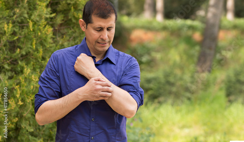 Obraz na plátně Man scratching arm because it stings in a park with copy space