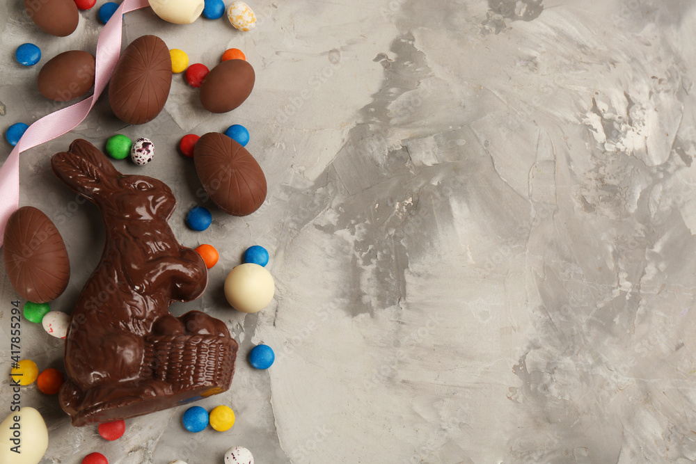 Flat lay composition with chocolate Easter bunny, eggs and candies on light grey table. Space for text