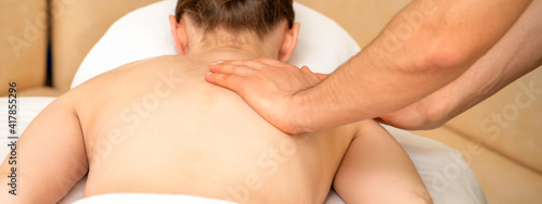 Hands of a masseur massaging back of a young adult woman in spa salon
