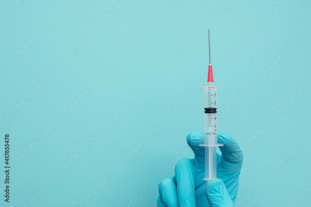 A doctor or nurse wearing blue surgical gloves holding a vaccine syringe A doctor or nurse wearing blue surgical gloves holding a vaccine syringe