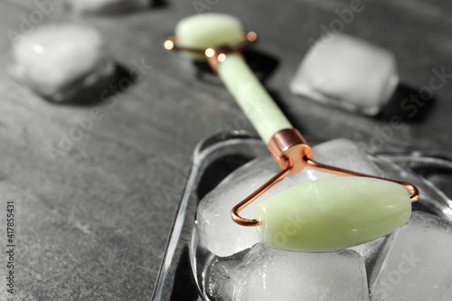 Fototapeta Naklejka Na Ścianę i Meble -  Natural jade face roller and ice cubes on grey background, closeup