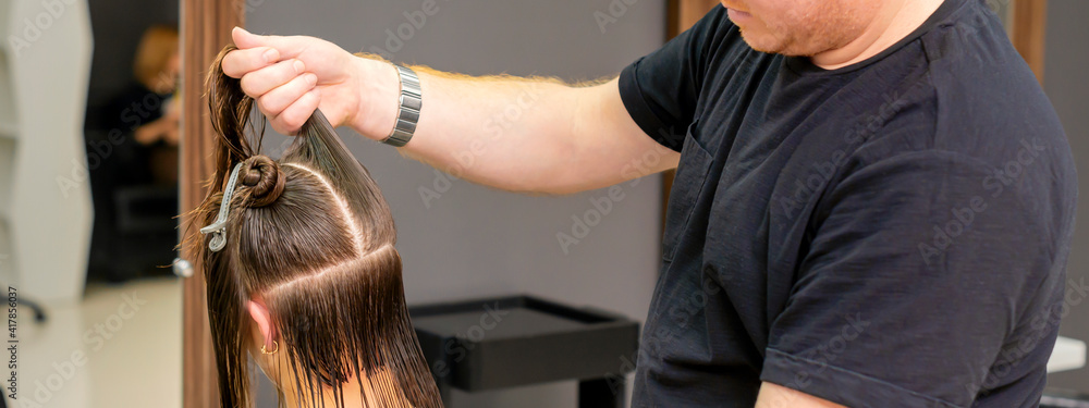 Fototapeta premium Male hairdresser holds and splits long hair of a young brunette woman in a hair salon