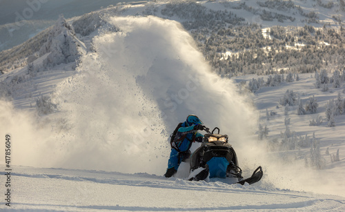 Pro snowmobiler makes a turn and lets a flurry of snow spray from under the caterpillar. sports snowmobile in the mountains. bright skidoo motorbike and suit without brands. Winter fun. panoramic view