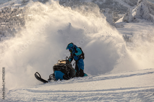 a guy on a mountain snowmobile skids and pushes full throttle, letting out large fountains of snow from under the tracks. bright skidoo motorbike and suit without brands. Winter fun. panoramic view