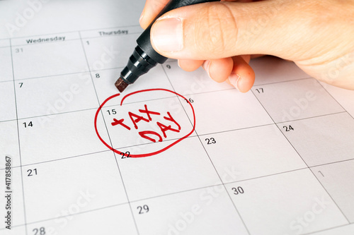 Writing tax day on April 15 calendar with red marker. Deadline for 1040 form return.