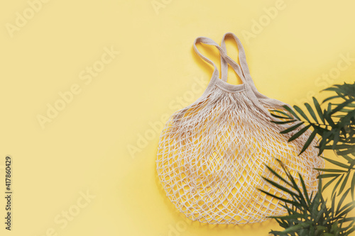 Empty reusable shopping string bag and green branches palm leaves on yellow background. Zero waste, eco-friendly. Mesh bag. Flat lay, top view, copy space
