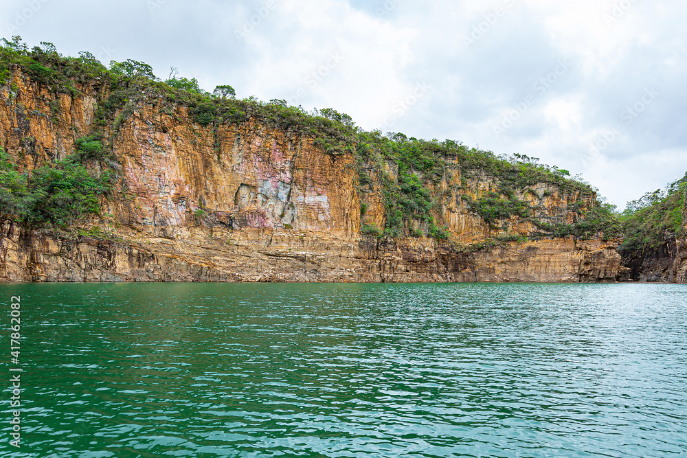 Rock walls with orange tones next to the lake and green vegetation growing on rocks of the Canyons of Furnas, Capitólio MG, Brazil.