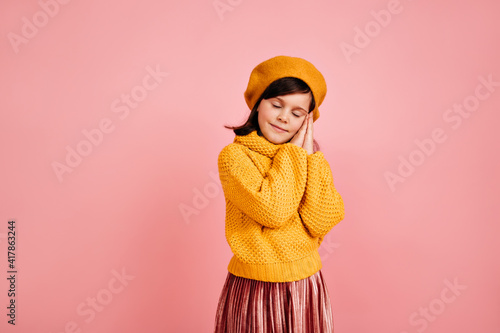 Sleepy brown-haired child standing on pink background. Studio shot of kid posing with eyes closed.