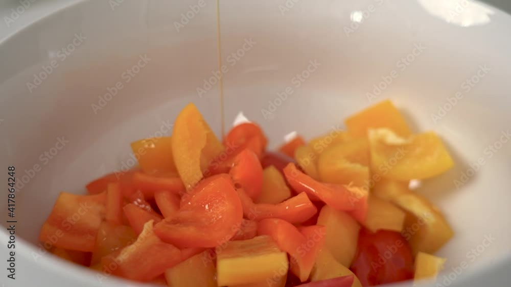 Olive oil dropping in slow motion into a porcelain white bowl that contains sliced orange and red bell peppers Olive oil dropping in slow motion into a porcelain white bowl that contains sliced orange and red bell peppers