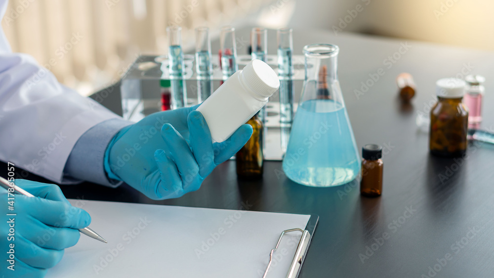 A medicine bottle in the hand of a doctor holding a doctor prescribing medicine to the patient the doctor sitting at the desk in the office with a vaccine trial bottle on the table A medicine bottle in the hand of a doctor holding a doctor prescribing medicine to the patient the doctor sitting at the desk in the office with a vaccine trial bottle on the table