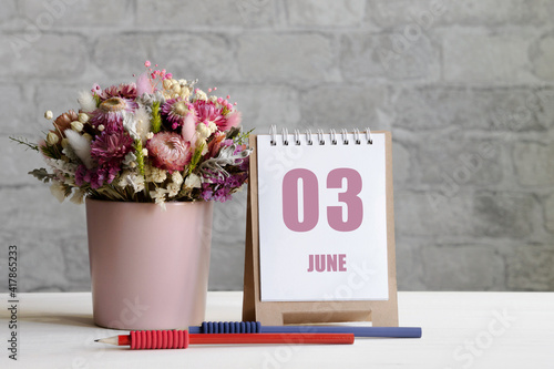 june 03. 03th day of the month, calendar date.A delicate bouquet of flowers in a pink vase, two pencils and a calendar with a date for the day on a wooden surface photo