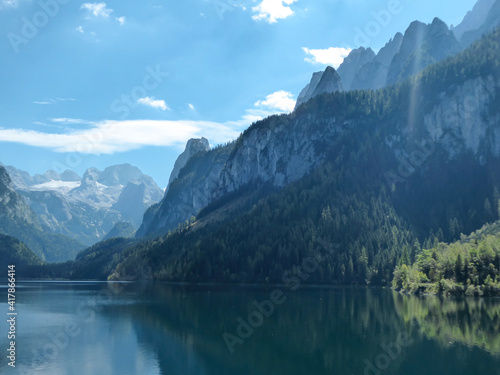 Panoramic view on Gosau lake, with Dachstein glacier in the back in Austrian Alps. The lake is surrounded by high mountains, overgrown with tall trees. Sun reflects on the surface. Serenity  and calm © Chris