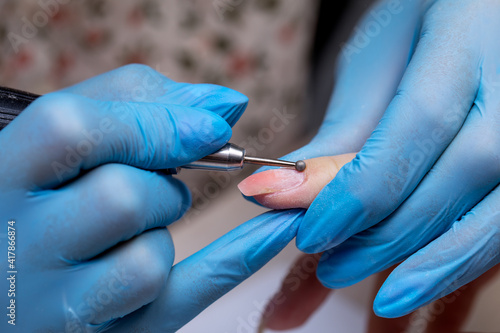 The manicurist cleans the cuticle on the nail with a round cutter. Hardware manicure in the salon.