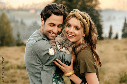Beautiful sensual couple hug together with the cat and smile cheerfully in nature. © Александр Шуневич