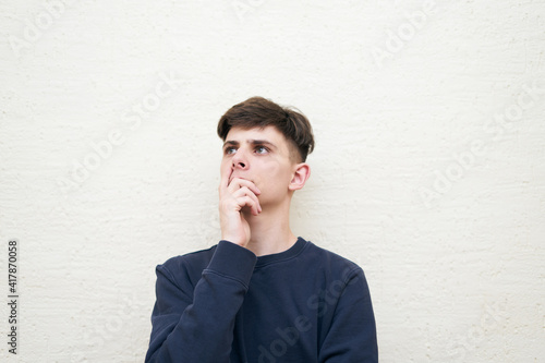 Pensive young man portrait in stylish clothes standing on wall background