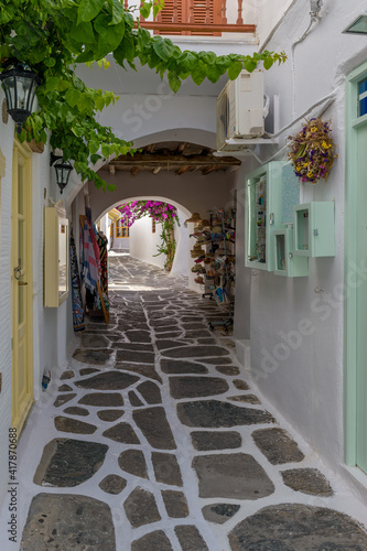 Fototapeta Naklejka Na Ścianę i Meble -  Traditional Cycladitic alley with narrow street, whitewashed facade of stores a cafe exterior and a blooming bougainvillea in Naousa  Paros island, Greece.