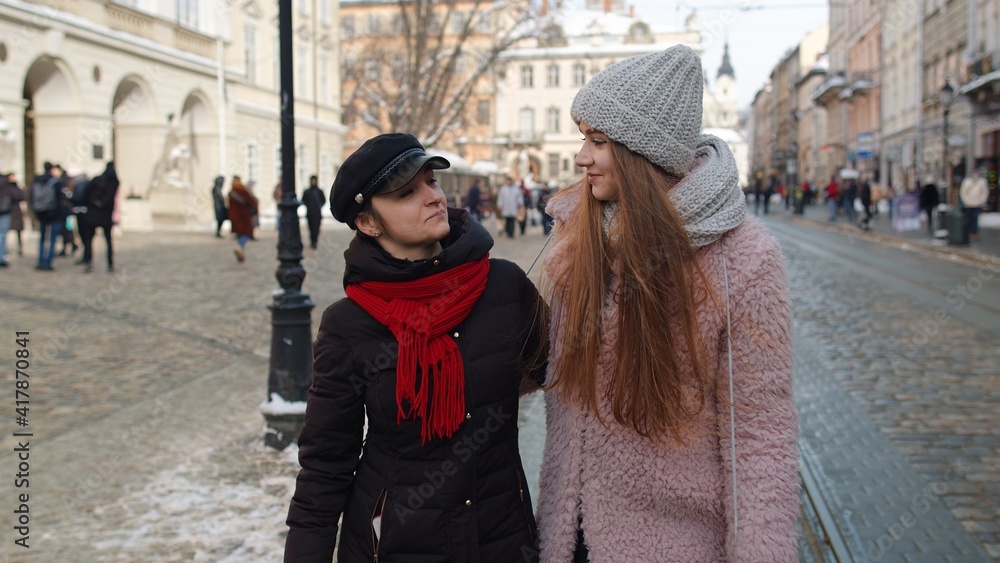 Two smiling women tourists walking together on city street. Family couple talking, embracing, having fun, looking at famous sights of old town. Winter holiday traveling. Concept of lesbian LGBT people