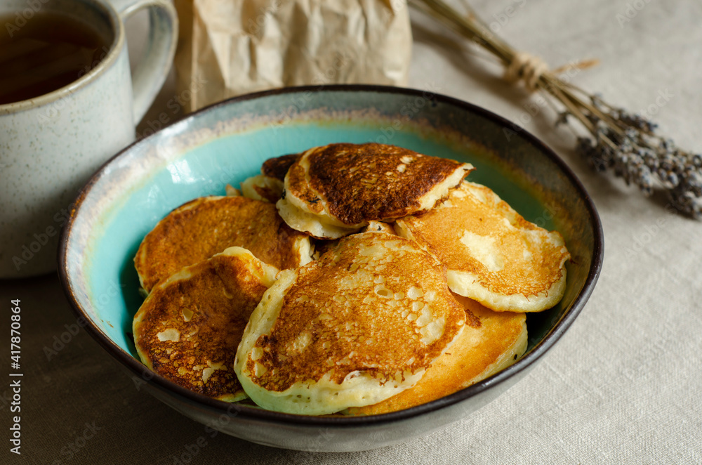 Fried kefir pancakes in a blue plate, lavender flowers and a mug with a drink. Fried kefir pancakes in a blue plate, lavender flowers and a mug with a drink.