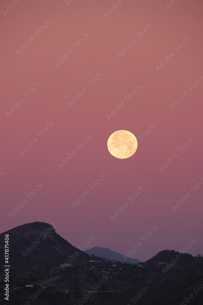 Paisaje en vertical con luna llena sobre unas montañas en el horizonte y un cielo rosado. Málaga, Spain Paisaje en vertical con luna llena sobre unas montañas en el horizonte y un cielo rosado. Málaga, Spain