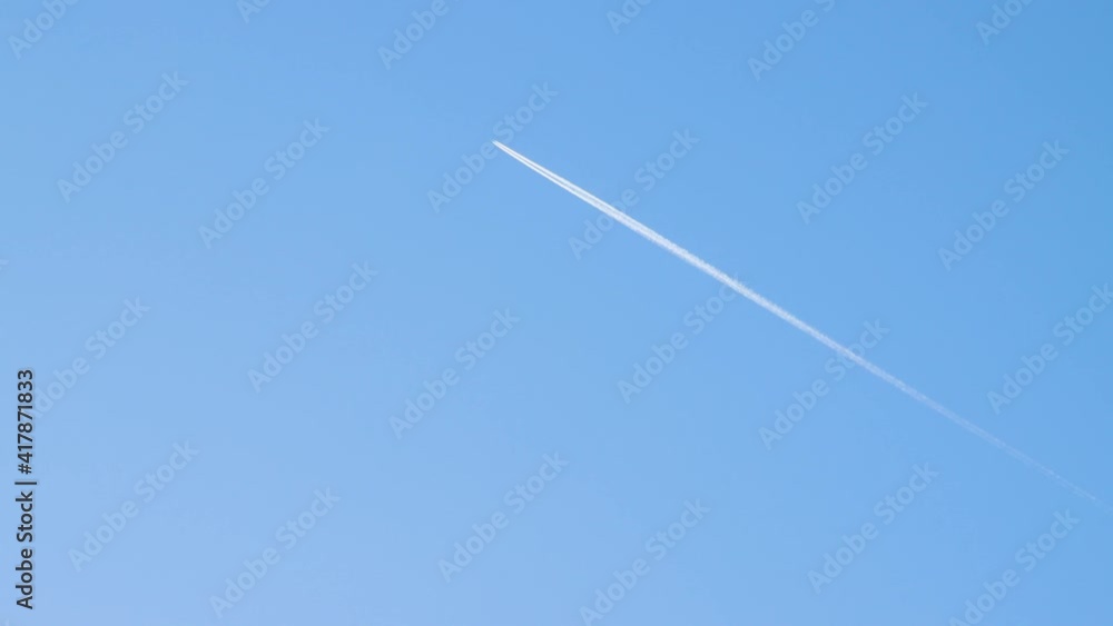 An airplane flies high above the ground leaving an even white trail. Blue sky, natural landscape illuminated by the sun. Beautiful background with clear weather and copy space. Time-lapse 4K video. An airplane flies high above the ground leaving an even white trail. Blue sky, natural landscape illuminated by the sun. Beautiful background with clear weather and copy space. Time-lapse 4K video.
