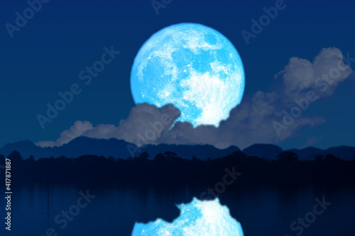 Super blue worm blue moon rise back silhouette mountain blur dark cloud on the night sky and reflection on water surface