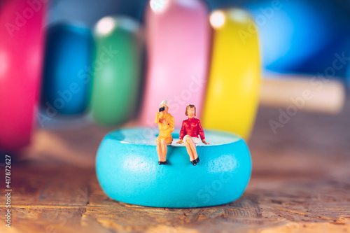 Miniature people, couple woman sitting on wooden block using as business and social distancing concept