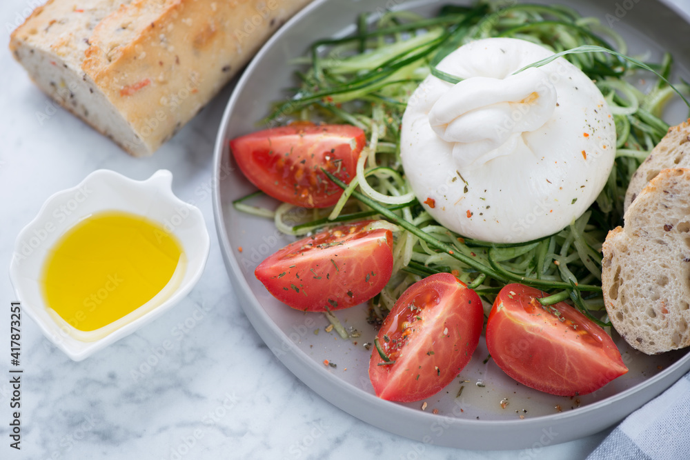 Closeup of salad with burrata cheese, cucumber and tomatoes served on a grey plate, horizontal shot, selective focus Closeup of salad with burrata cheese, cucumber and tomatoes served on a grey plate, horizontal shot, selective focus
