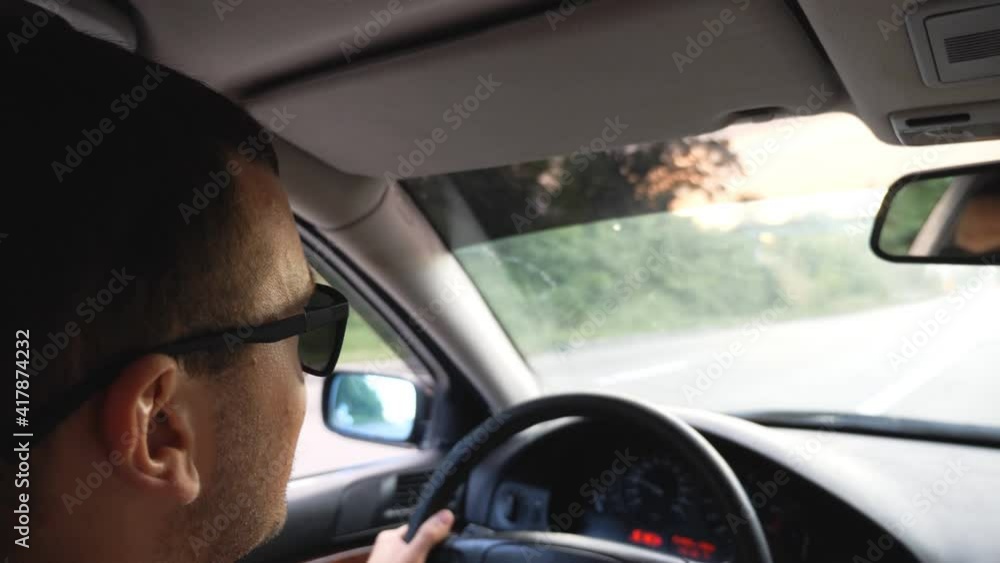 Unrecognizable man in sunglasses driving car on highway. Young confident guy looking to road during controlling auto. Back view from vehicle salon. Concept of road trip. Slow motion Unrecognizable man in sunglasses driving car on highway. Young confident guy looking to road during controlling auto. Back view from vehicle salon. Concept of road trip. Slow motion