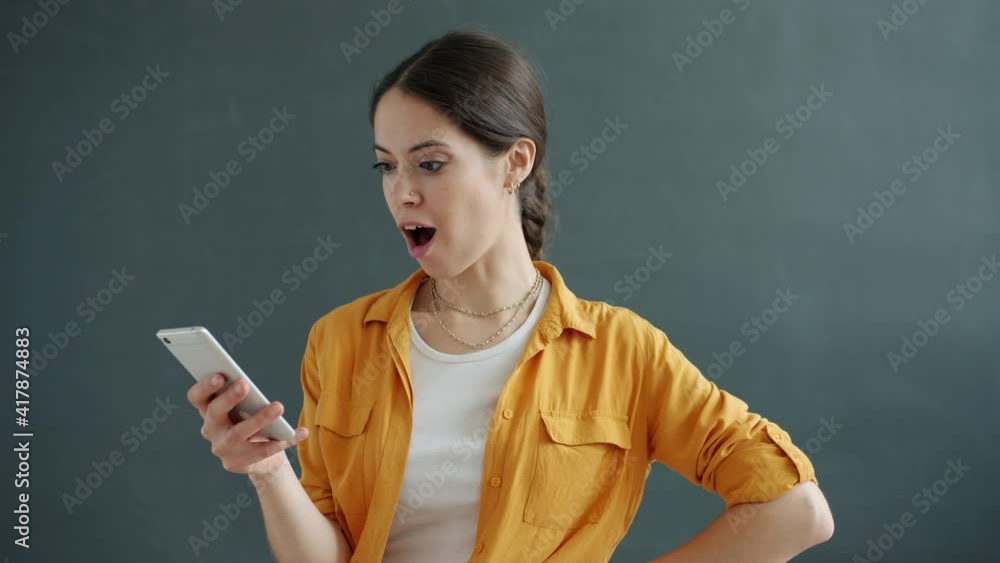 Portrait of cheerful young lady looking then pointing at smartphone screen and showing thumbs-up hand gesture. Applications and online content concept. Portrait of cheerful young lady looking then pointing at smartphone screen and showing thumbs-up hand gesture. Applications and online content concept.
