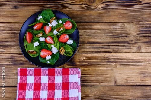 Salad with spinach leaves, feta cheese, walnuts and strawberry on a black plate. Top view