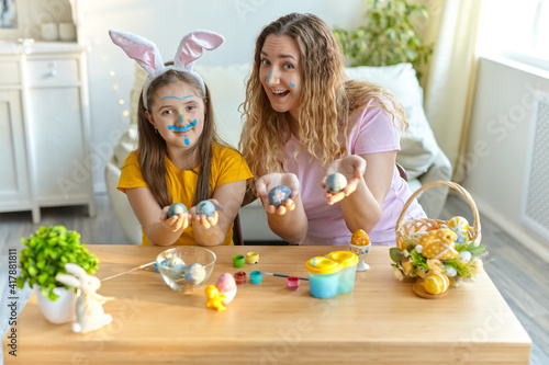 Mother and her daughter painting eggs. Happy family preparing for Easter.