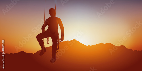 Concept de sport extrême, avec un alpiniste suspendu à une parois par des corde devant un coucher de soleil sur une chaine de montagne.
