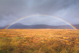 A full colourful rainbow in a moody countryside landscape near Glencoe in the Scottish Highlands, Scotland.