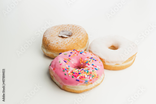 Three fresh, colourful ring doughnuts isolated on a plain white surface and background.