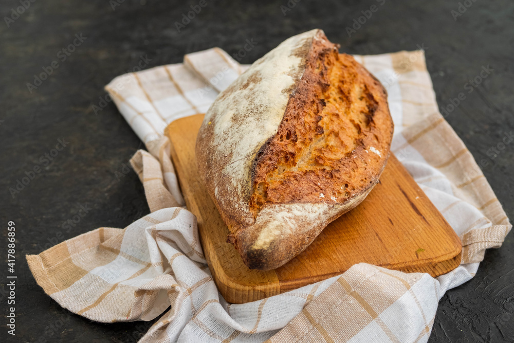 A whole loaf of homemade wheat bread on a wooden board against a dark concrete background. A whole loaf of homemade wheat bread on a wooden board against a dark concrete background.
