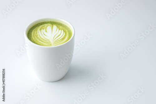 White porcelain cup without handle, patterned matcha latte, white matte background.